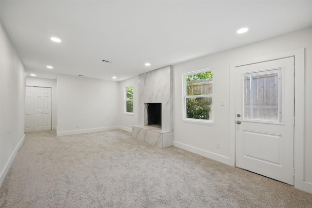 unfurnished living room featuring light colored carpet, a high end fireplace, baseboards, and recessed lighting