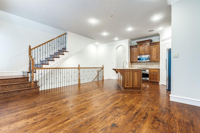 kitchen featuring ornamental molding, dark wood finished floors, appliances with stainless steel finishes, and a breakfast bar area