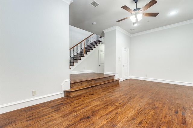 unfurnished living room featuring a ceiling fan, visible vents, wood finished floors, ornamental molding, and stairs