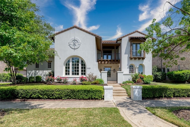 mediterranean / spanish-style home with a tiled roof, a fenced front yard, a gate, a balcony, and stucco siding
