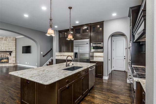 kitchen featuring arched walkways, a sink, appliances with stainless steel finishes, and dark wood finished floors