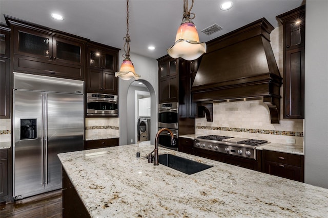 kitchen with stainless steel appliances, backsplash, visible vents, a sink, and custom range hood