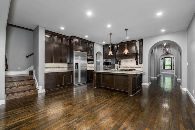 kitchen featuring custom exhaust hood, arched walkways, dark brown cabinetry, stainless steel appliances, and dark wood-style floors