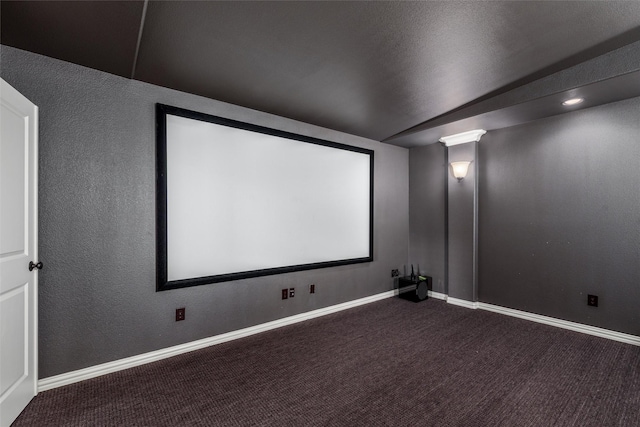 carpeted home theater featuring a textured wall and baseboards
