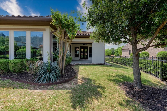 rear view of house with fence, a tiled roof, stucco siding, ceiling fan, and a lawn