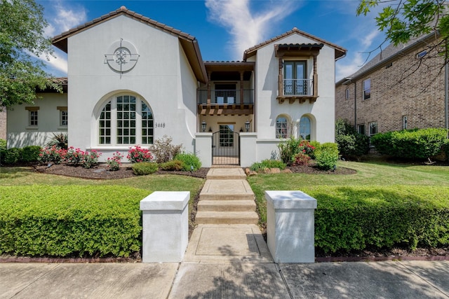 mediterranean / spanish home featuring a tile roof, a front lawn, a gate, a balcony, and stucco siding