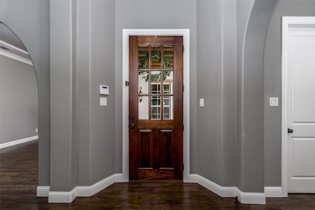 foyer featuring arched walkways, wood finished floors, and baseboards