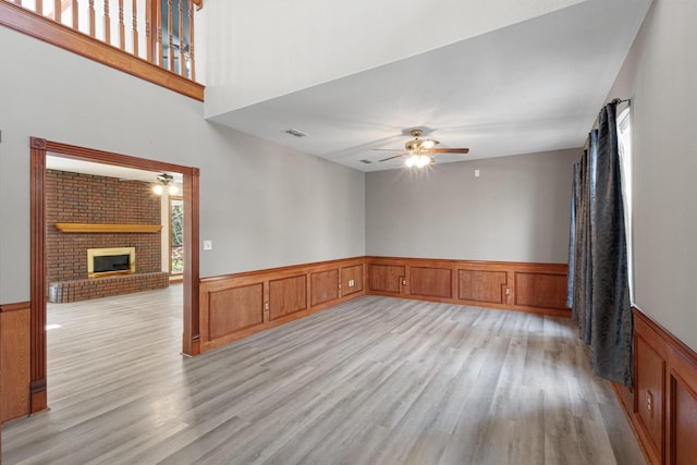 516 Wild Wood Dr, Decatur, TX 76234 - spare room featuring ceiling fan, a wainscoted wall, light wood finished floors, and a brick fireplace