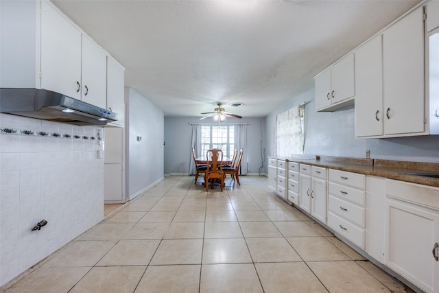 kitchen with dark countertops, white cabinetry, a ceiling fan, under cabinet range hood, and light tile patterned floors