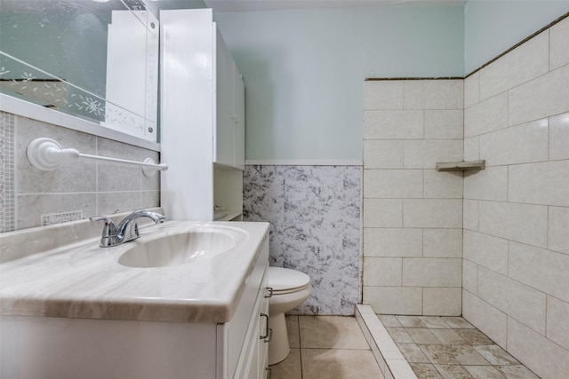 bathroom with tile patterned floors, a wainscoted wall, toilet, vanity, and tile walls