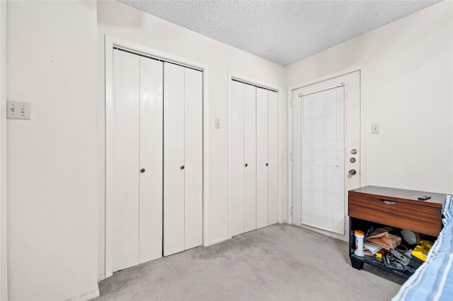 bedroom with two closets, a textured ceiling, and light colored carpet
