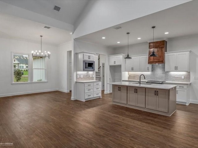 kitchen featuring stainless steel microwave, decorative backsplash, a sink, and white cabinets