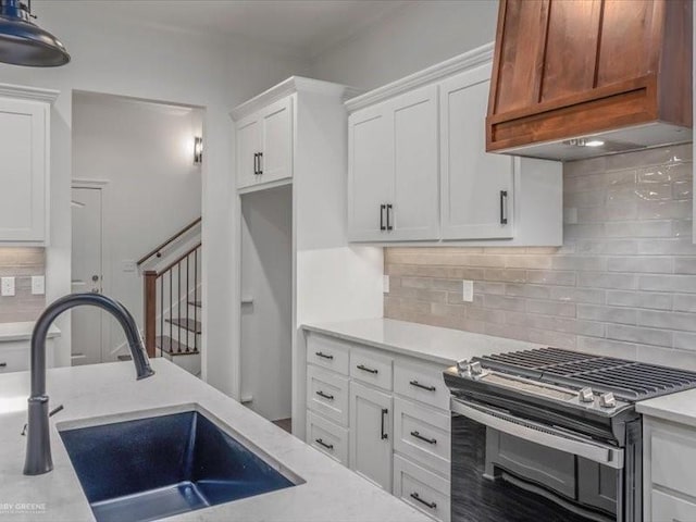 kitchen featuring a sink, white cabinets, premium range hood, backsplash, and stainless steel gas range oven