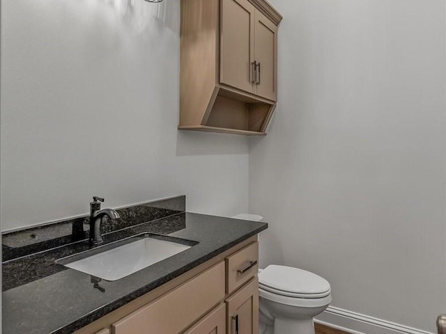half bathroom featuring baseboards, vanity, and toilet