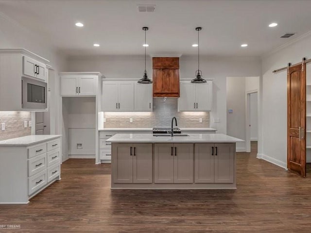 kitchen featuring a barn door, a sink, light countertops, backsplash, and visible vents