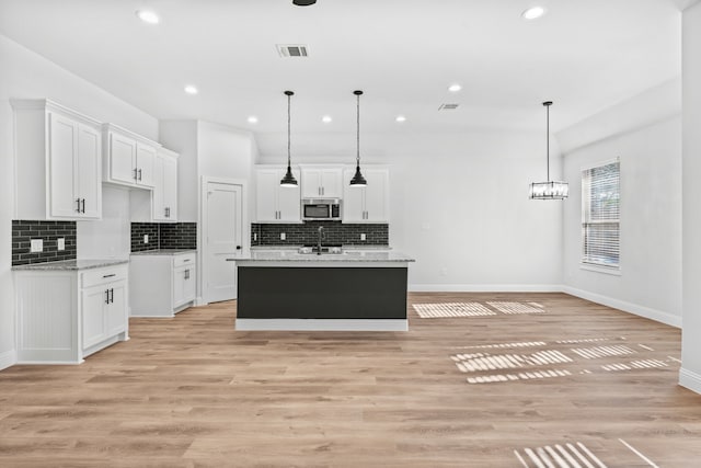kitchen with stainless steel microwave, white cabinets, baseboards, and a sink