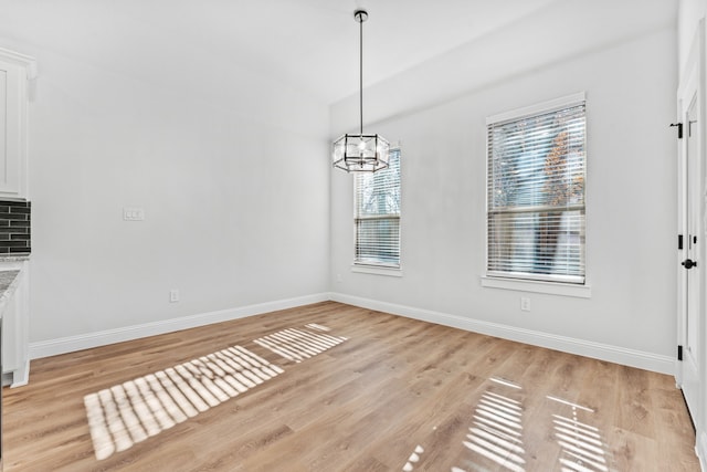 unfurnished dining area with baseboards, light wood finished floors, and an inviting chandelier