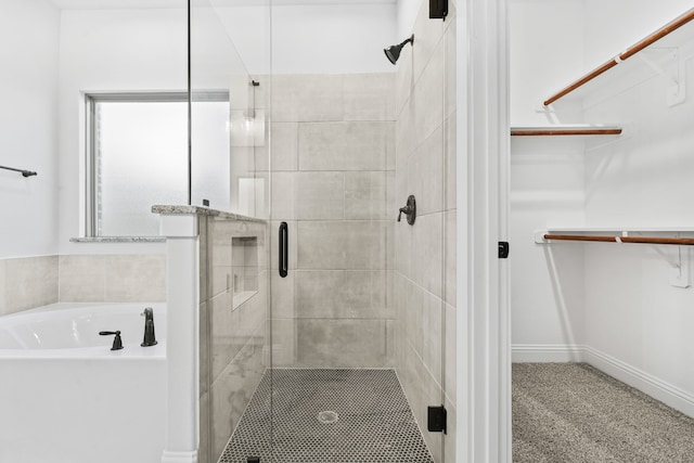 bathroom featuring a walk in closet, a bath, a shower stall, and baseboards