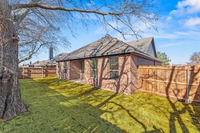 view of side of property with a shingled roof, a lawn, a fenced backyard, and brick siding