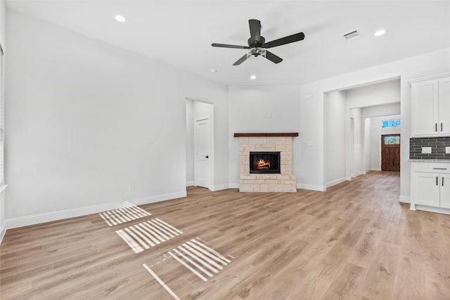 unfurnished living room featuring light wood-style flooring, baseboards, visible vents, a ceiling fan, and a fireplace