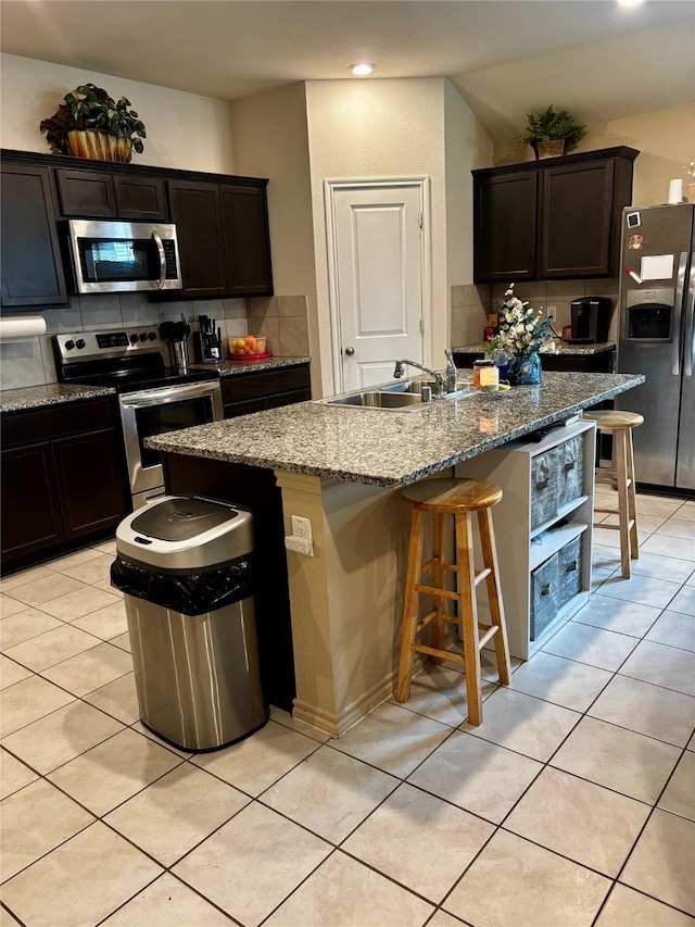 828 Costlow Ln, Fate, TX 75189 - kitchen featuring appliances with stainless steel finishes, a kitchen bar, light tile patterned floors, a kitchen island with sink, and stone counters