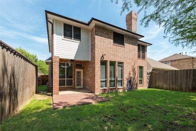 back of property with a chimney, a fenced backyard, a yard, a patio, and brick siding