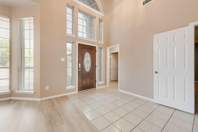 entrance foyer featuring visible vents, light wood finished floors, baseboards, and a towering ceiling