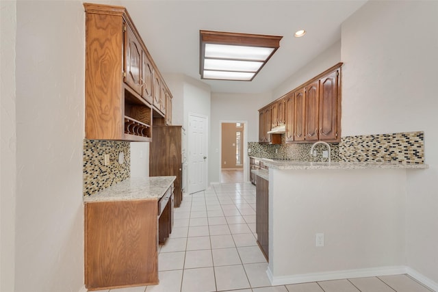 kitchen with under cabinet range hood, baseboards, decorative backsplash, and light tile patterned floors