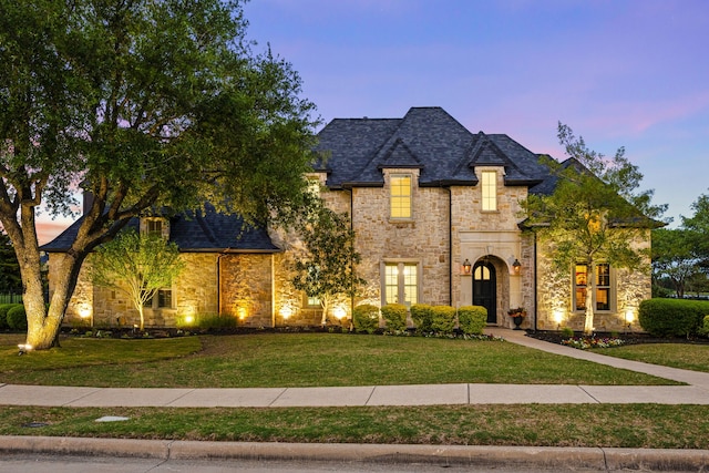 french country inspired facade with stone siding and a front lawn