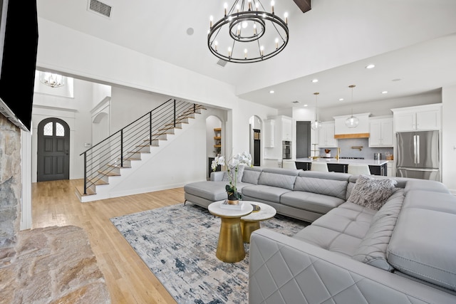 living room with stairway, an inviting chandelier, visible vents, light wood-type flooring, and high vaulted ceiling