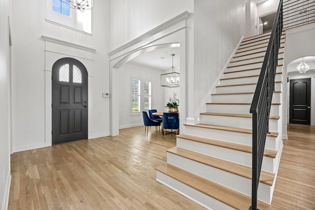 foyer with arched walkways, an inviting chandelier, wood finished floors, a high ceiling, and stairs