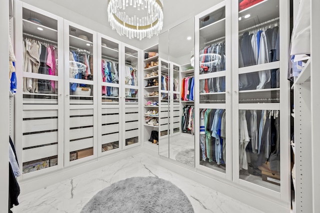 walk in closet featuring marble finish floor and an inviting chandelier