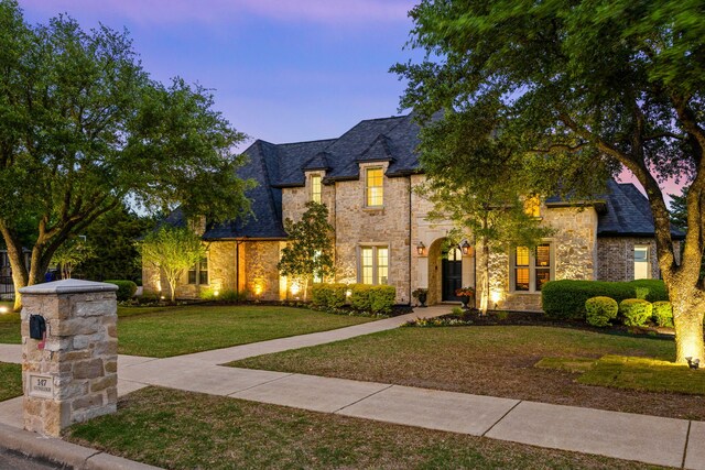 french country home with a lawn and stone siding