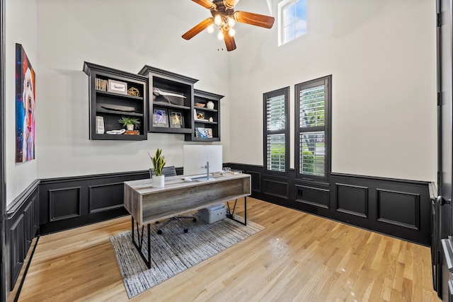 office space featuring light wood finished floors, a ceiling fan, and a wainscoted wall