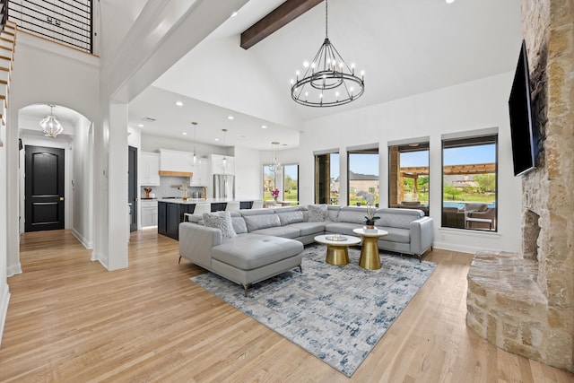 living room with arched walkways, light wood-style floors, a notable chandelier, beamed ceiling, and high vaulted ceiling