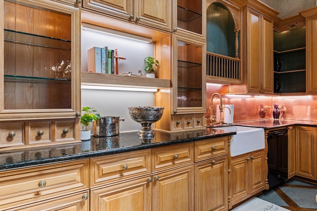 kitchen featuring glass insert cabinets, a sink, decorative backsplash, and dark stone counters