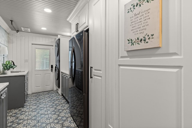 kitchen featuring stacked washer / dryer, light tile patterned floors, light countertops, white cabinetry, and freestanding refrigerator