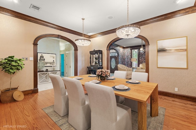 dining room with arched walkways, ornamental molding, light wood-style floors, and visible vents