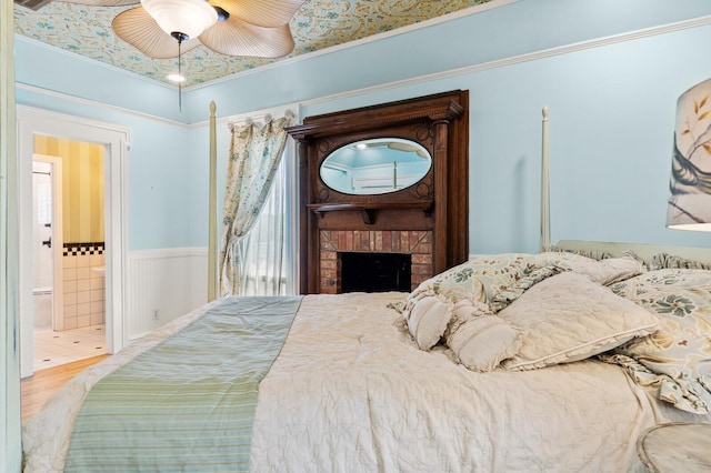 bedroom featuring a wainscoted wall, wood finished floors, connected bathroom, crown molding, and ceiling fan