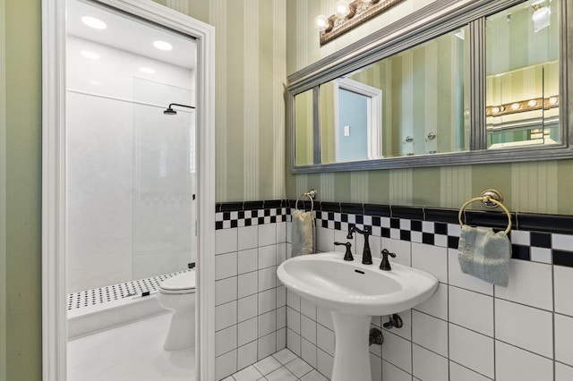 bathroom with wallpapered walls, toilet, a stall shower, and wainscoting