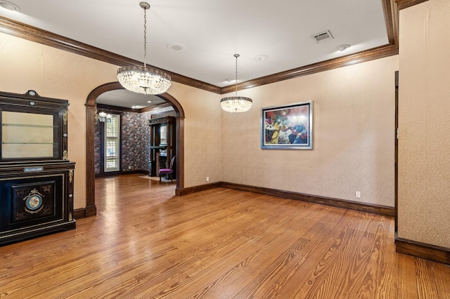 unfurnished dining area with crown molding, arched walkways, light wood finished floors, baseboards, and visible vents