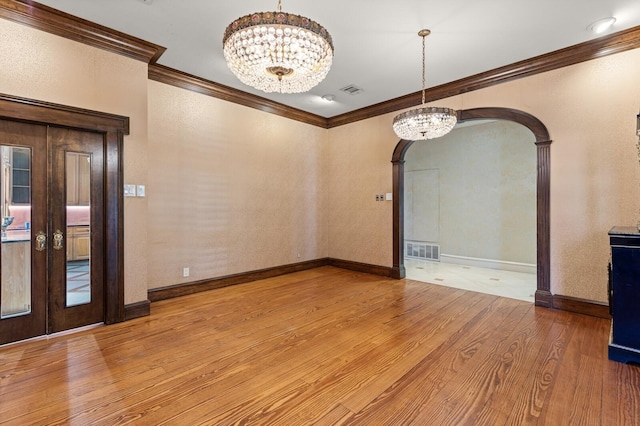empty room with arched walkways, visible vents, a notable chandelier, wood finished floors, and ornamental molding