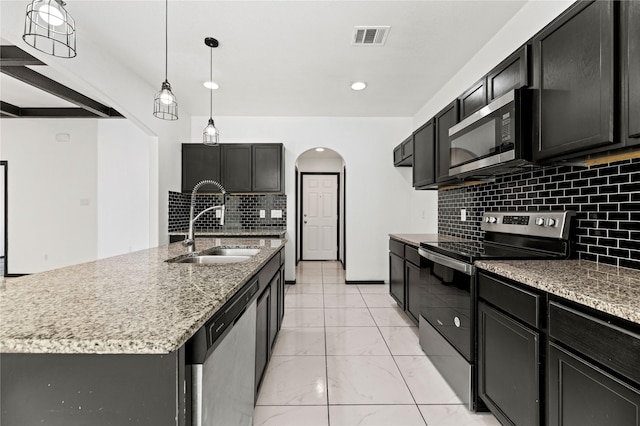 kitchen featuring a sink, arched walkways, light stone countertops, decorative backsplash, and appliances with stainless steel finishes