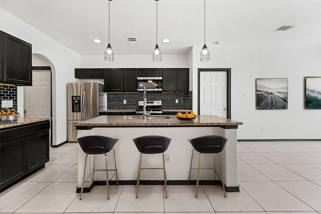 kitchen with a sink, dark cabinets, a breakfast bar area, marble finish floor, and appliances with stainless steel finishes