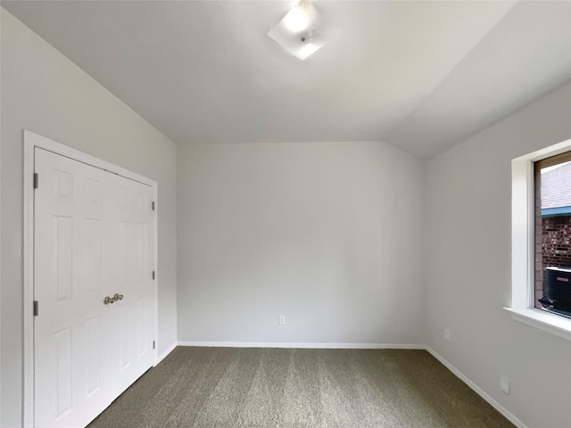 empty room featuring lofted ceiling, dark colored carpet, and baseboards