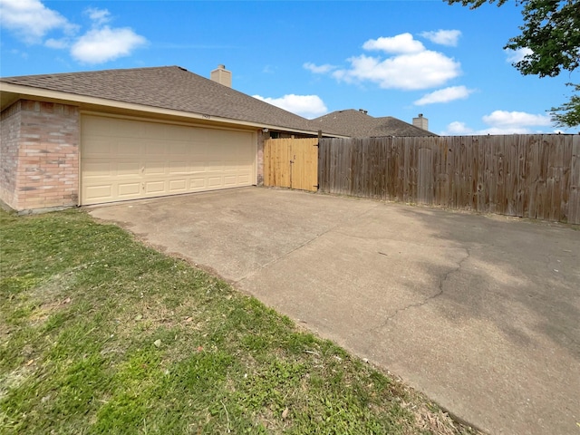view of side of property with a chimney, fence, an attached garage, driveway, and brick siding