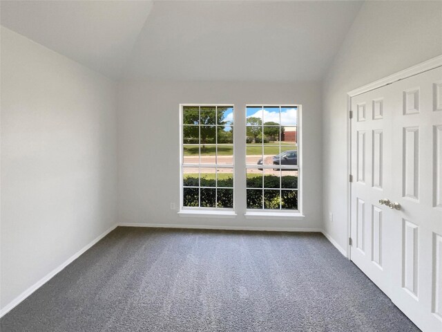 spare room featuring vaulted ceiling, baseboards, and dark colored carpet