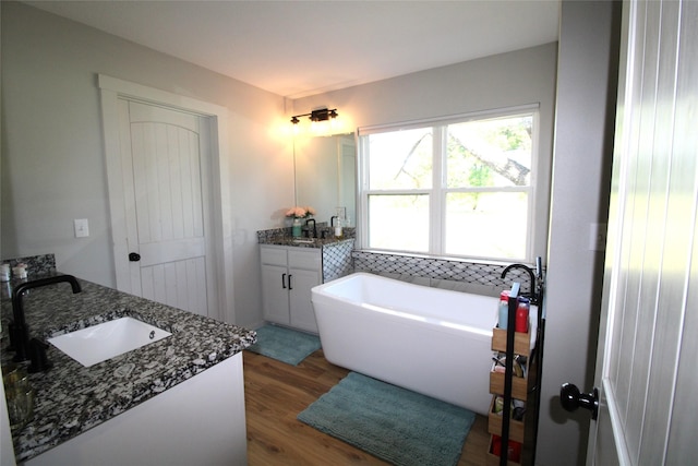 full bathroom featuring two vanities, wood finished floors, a soaking tub, and a sink