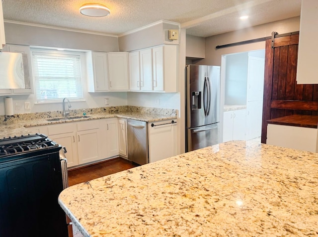 kitchen with light stone counters, a textured ceiling, a sink, stainless steel appliances, and white cabinets