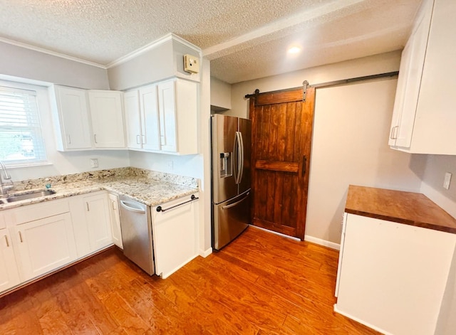 kitchen with white cabinets, a sink, a textured ceiling, wood finished floors, and appliances with stainless steel finishes